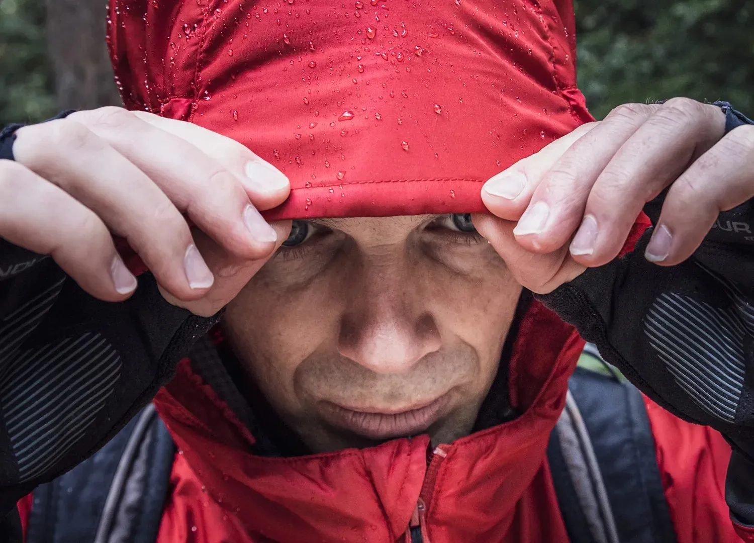 Man pulling down the hood of a wet red jacket